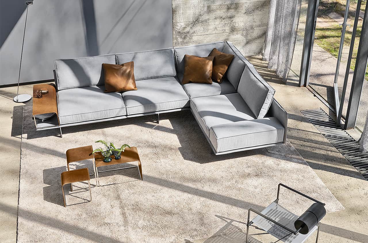 Graues Ecksofa mit klaren Linien, rechteckigen Polstern und offener, lichtdurchfluteter Wohnumgebung mit Betonoptik.